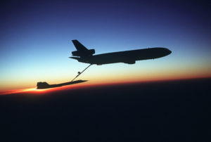 A right side view of a KC-10 Extender aircraft refueling an SR-71 Blackbird aircraft in-flight during testing. The Extender, silhouetted against the sunset horizon, is from the 78th Air Refueling Squadron, and the Blackbird, the 9th Strategic Reconnaissance Wing.